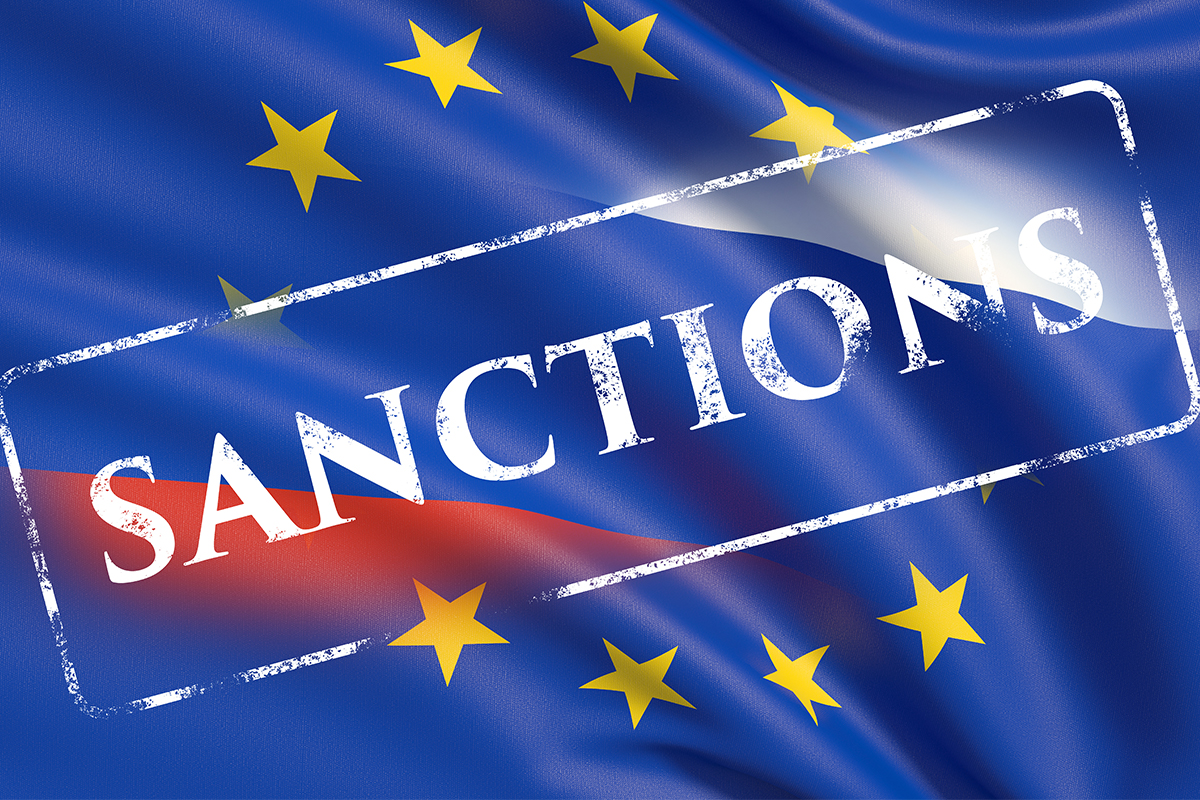 Eine EU-Flagge vor einer Russland-Flagge und davor ein weißer Stempel mit Aufschrift „Sanctions